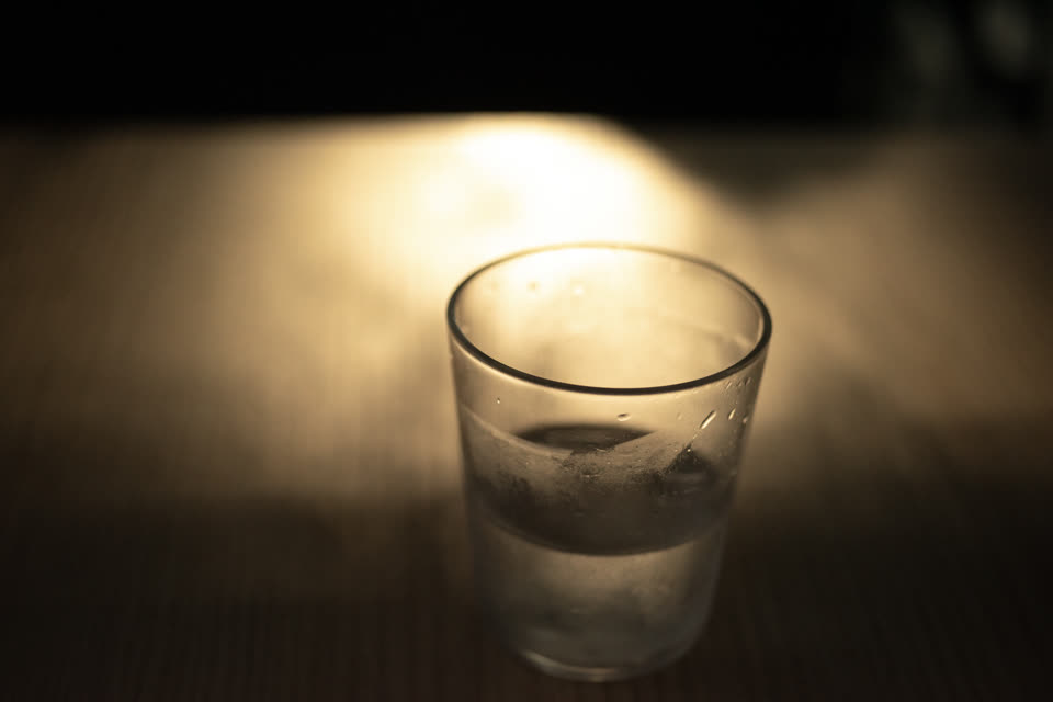 暗い机の上、電球色の光に照らされた水の入ったグラス