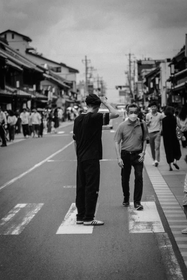 白黒。古い町並みの横断歩道。人通りの中で一人だけ立ち止まっている